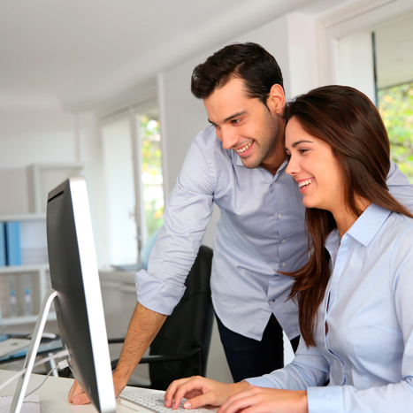 Dos personas en un ambiente laboral observan la pantalla de un computador de escritorio.