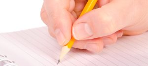 Mano con lápiz escribiendo en una hoja de papel.