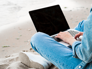 Persona sentada en la playa con computador portátil