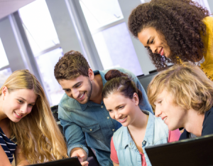 Cinco estudiantes reunidos en frente a dos computadores teclados.