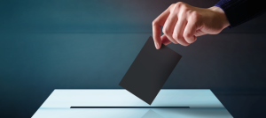 Mano insertando un voto en una urna de votación.