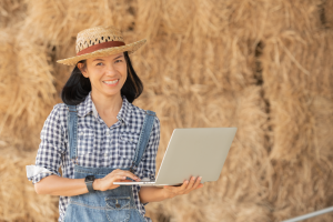 Mujer con overall y sombrero sosteniendo un equipo portátil con sus manos.