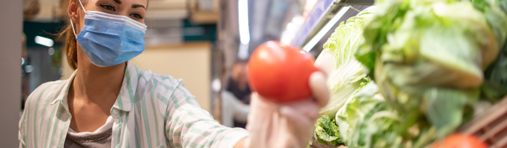 Mujer con medidas de protección sosteniendo un tomate en su mano izquierda.