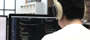 Joven frente a una gran pantalla de computador escribiendo en algún lenguaje de programación.