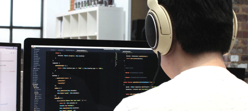 Joven frente a una gran pantalla de computador escribiendo en algún lenguaje de programación.