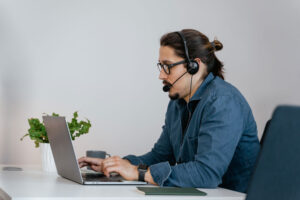Hombre con auriculares y gafas en frente de un computador portátil.