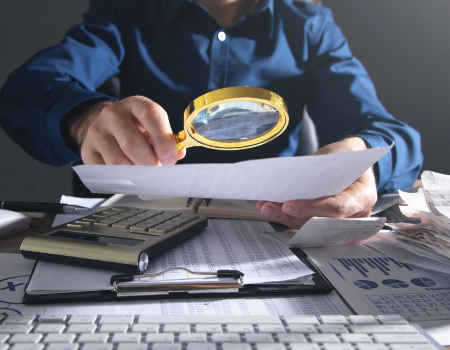 Hombre con una lupa registra estados contables en un ambiente corporativo.